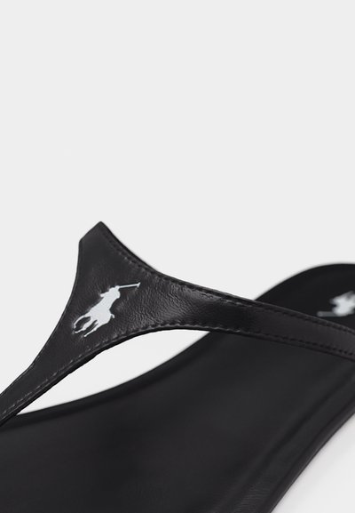 Detailní záběr černého koženého pásku na žabce s vyraženým bílým logem hráče póla.