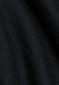 Gros plan sur un tissu tricoté noir doux avec une texture côtelée visible et des plis subtils créant un contraste de lumière et d'ombre.