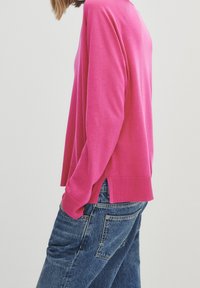 Pull en tricot fuchsia avec un col rond, des poignets côtelés et des fentes latérales, associé à un jean en denim bleu taille haute.
