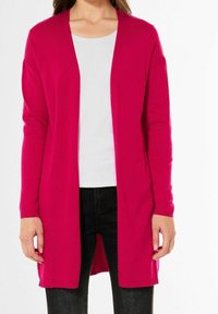 Långärmad cardigan i lysande fuchsia, med öppen frontdesign, lättstickad textur, matchad med en vit topp och mörka jeans.