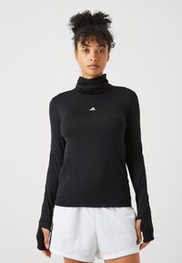 Schwarzes Langarmoberteil mit hohem Kragen und Daumenlöchern, aus glattem Stoff gefertigt. Verfügt über ein kleines weißes Logo auf der Brust.