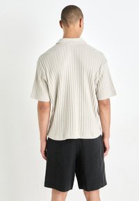 Kortærmet beige ribbet skjorte med detaljer ved rygkraven, parret med sorte shorts. Sættet har en afslappet pasform og blød tekstur.