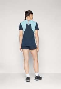 Marinblå och ljusblå sporttopp med korta ärmar, med en triangel-design på ryggen och en röd accent i mitten. Bärs med matchande shorts.