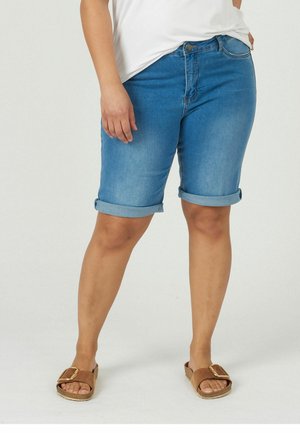 Blå denimshorts med uppvikta ben, med knappknäppning framtill och bältesöglor, kombinerat med bruna sandaler med spänne.