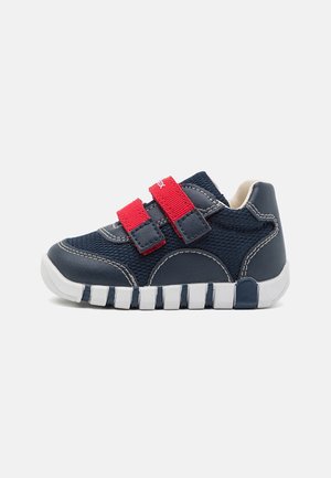 Baskets bleu marine avec des bandes Velcro rouges, tige en tissu texturé, col rembourré et une semelle en caoutchouc blanc épaisse et segmentée.