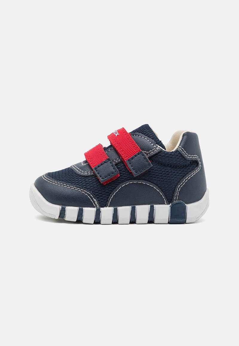Sneaker blu navy con cinturini in velcro rossi, upper in tessuto strutturato, colletto imbottito e suola in gomma bianca spessa e segmentata.
