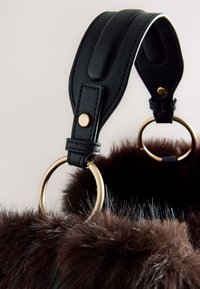 Curea neagră din piele cu accesorii aurii atașată unei genți maro din blană faux. Caracteristici includ un finisaj texturat și inele rotunde pentru prindere.