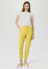 White short-sleeve top with lace trim, paired with yellow tailored trousers and light beige pointed flats. Simple, modern, and solid colors.