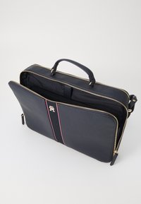 Borsa per laptop in pelle blu scuro con zip dorate, doppie maniglie e un compartimento interno. Presenta un accento a strisce e un dettaglio del logo.