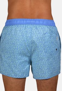 Des shorts de bain à motifs bleus présentent une taille élastique bleu clair et une poche arrière. Le design inclut des formes ressemblant à des coraux dans des nuances de bleu variées.