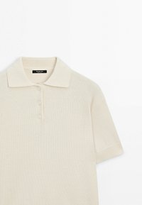 Beige Poloshirt mit kurzen Ärmeln, strukturierter Strickware, Knopfleiste mit drei Knöpfen sowie geripptem Kragen und Bündchen. Markenlabel innen am Kragen sichtbar.