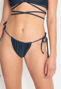 Navyblå bikiniunderdel med en rynkad framsida, justerbara sidband och en minimal täckning, tillverkad av mjukt, elastiskt tyg.