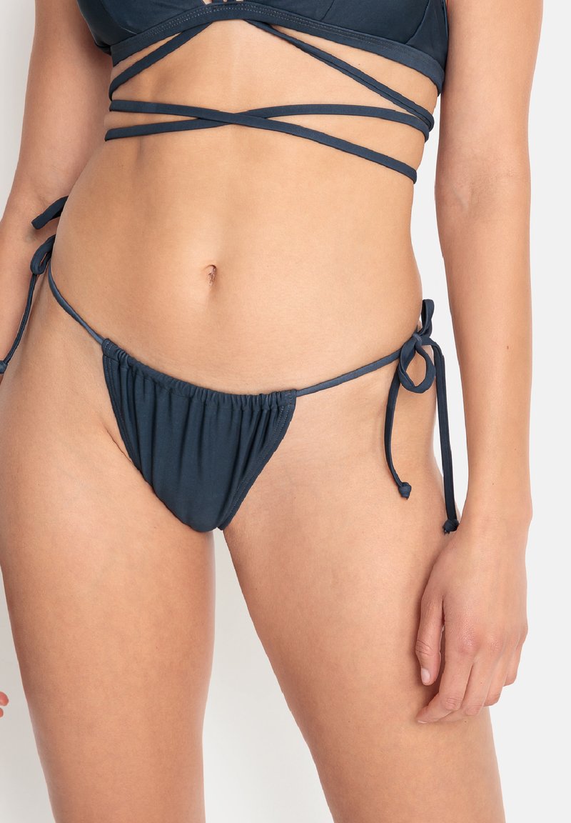 Navyblå bikiniunderdel med en rynkad framsida, justerbara sidband och en minimal täckning, tillverkad av mjukt, elastiskt tyg.