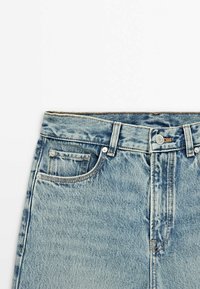 Partie taille d'un jean en denim bleu clair avec bouton devant, fermeture éclair, passants de ceinture et poches avant et pour la monnaie visibles.
