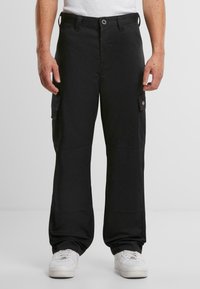 Svarta cargobyxor i tåligt tyg, med sidofickor, avslappnad passform och knappstängning. Bärs med vita sneakers.