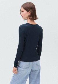 Námořnická modrá tričko s dlouhým rukávem a žebrovaným vzorem s kulatým výstřihem, doplněné o světlé modré kalhoty s širokými nohavicemi, které se vyznačují uvolněným střihem a měkkou texturou.