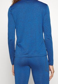 Maglia sportiva a maniche lunghe blu con una texture mélange. Presenta un collo rotondo e un retro leggermente allungato per una maggiore copertura.