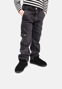 Pantalones cargo negros con múltiples bolsillos, detalles metálicos y un ajuste cómodo, combinados con botas de tobillo negras y texturizadas.