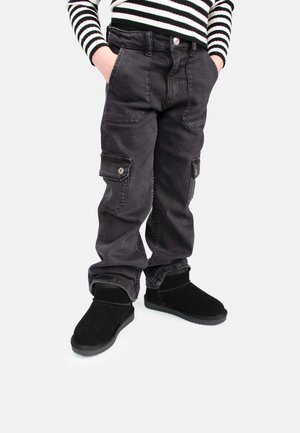 Schwarze Cargo-Hosen mit mehreren Taschen, metallischen Akzenten und einem bequemen Schnitt, kombiniert mit schwarzen, strukturierten Stiefeletten.