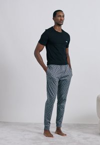 Fekete rövid ujjú póló szürke mintás, geometriai mintával és elasztikus mandzsettákkal rendelkező joggerral párosítva. A modell mezítláb áll.