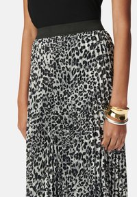 Falda plisada de estampado de leopardo en negro y gris con una cinturilla elástica negra. Brazaletes de plata y oro adornan la muñeca.