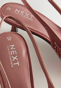 Vaaleanpunaiset korkeakorkoiset sandaalit satiinivöillä, pehmustetulla pohjalla ja koristeellisilla yksityiskohdilla. Sisältää hopeisen brändilogon "NEXT". Koko 6½/40.