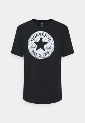 Zwart T-shirt met korte mouwen, met een wit rond Converse All Star-logo en kleurrijk verfspattingsontwerp aan de voorkant.