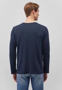 Navyblaue Langarmbluse mit gerippter Textur, rundem Halsausschnitt und genähten Säumen, kombiniert mit hellblauen Jeans.