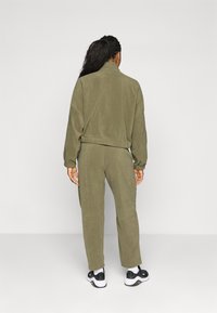 Olijfgroene fleece trainingsbroek met een hoge kraag en elastische manchetten, gecombineerd met zwart-witte sportschoenen. Soepele textuur, casual ontwerp.