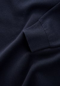 Tessuto lavorato a maglia blu navy scuro che mostra il polsino di una manica lunga con texture a coste e materiale del corpo liscio.