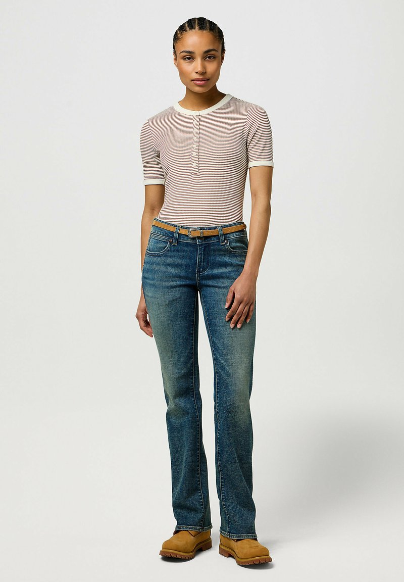 Randig kortärmad topp med knäppning, blå jeans med lätt blekning och bruna träskor, vilket skapar en avslappnad outfit.
