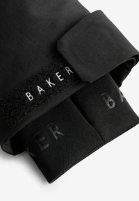 Mustat kankaiset hansikkaat, joissa on tarranauha ja valkoiset "BAKER"-kirjaimet; sileä pinta; näkyvissä kaksi suljettua sormikoloa.