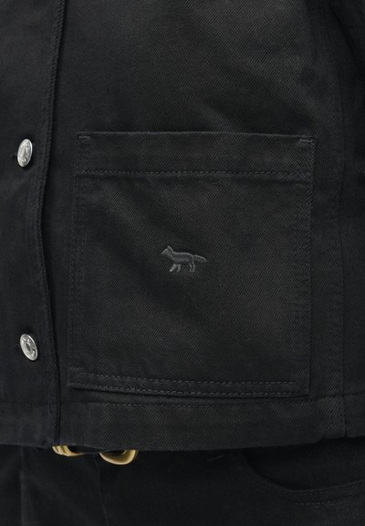 Mustmustest must jacket tasku, millel on väikene tikitud rebase logo sama värvi niidiga, vasakul pool hõbedane metallnupp.