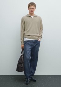 Beige gebreid trui met een kraag, gelaagd over een wit shirt, gecombineerd met donkerblauwe spijkerbroek en zwarte leren schoenen, met een donkere tas.