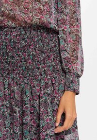 Blomsterprintkjole med gennemsigtig stof, der har en smocket talje, lange ærmer og en blanding af pink, lilla og grønne farver.