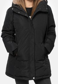 Svart puffjacka med foder i päls på huvan, frontdragkedja, sidofickor och justerbara dragskor. Har en lång, lätt böjd nederkant.