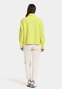Keltainen pörröinen pullover-takki, rento malli, jossa on korkea kaulus. Vaatteen alla pitkähihaisena paita ja yhdistettynä kermavärisiin housuihin sekä tennareihin.