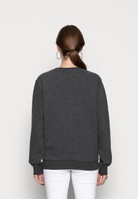 Felpa grigia scuro con maniche lunghe, polsini e orlo a coste, texture morbida e scollo rotondo. Indossata sopra pantaloni bianchi.