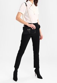 Pantalones de tiro alto negros, con silueta ajustada, combinados con una blusa blanca con cuello de lazo. Bolso negro con cadena y detalles decorativos.