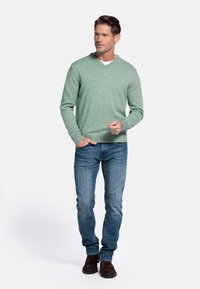 Lichtgroene v-hals trui in een gestructureerde brei, gecombineerd met blauwe jeans en bruine suède schoenen. De trui heeft ribgebreide manchetten en onderkant.