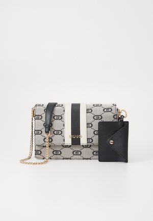 Sac bandoulière rectangulaire beige et noir à motif, avec bandoulière chaîne dorée, étiquette en cuir noir et détail rayé vertical noir et blanc.