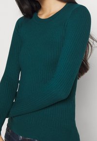 Sweter dzianinowy w kolorze morskim z prążkowaną fakturą, długimi rękawami, okrągłym dekoltem i dopasowanym dołem; wykonany z miękkiego materiału o teksturowanym wykończeniu.