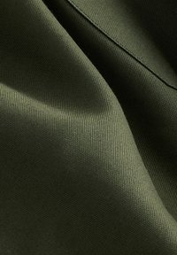 Tissu olive texturé avec une finition lisse, présentant un motif subtil et un léger éclat, affichant de multiples couches et plis.