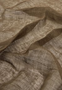 Przezroczysty brązowy materiał o pomarszczonej teksturze i delikatnym, siatkowym splocie. Miękki, lekki i lekko przezroczysty.