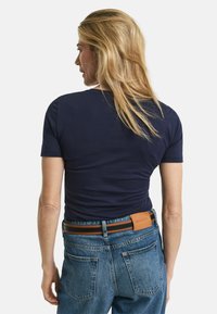 Marineblaue kurzärmlige T-Shirt mit taillierter Passform, kombiniert mit hochgeschnittenen hellen Jeans. Brauner und orange gestreifter Gürtel mit Logo.
