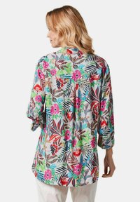 Blumenbluse mit 3/4-Ärmeln. Leichter, mehrfarbiger Stoff mit großen rosa Blumen, Blättern und Tiermustern. Lockere Passform, runder Saum.