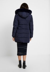 Navy puffer coat with a faux fur hood, featuring horizontal stitching and a slightly elongated back, paired with a ribbed skirt and black ankle boots.