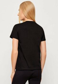 Czarny bawełniany t-shirt z krótkimi podwiniętymi rękawami, okrągłym dekoltem i luźnym krojem. Gładka tekstura, bez widocznych wzorów ani grafik.