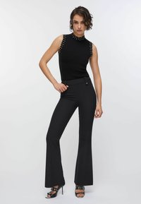 Haut noir sans manches avec accents cloutés sur les épaules, associé à un pantalon noir évasé et des sandales à talons à lanières. Tissu lisse.