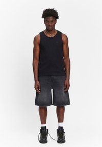 Black cotton tank top with a subtle logo, paired with dark denim shorts and black lace-up boots. Smooth texture throughout.